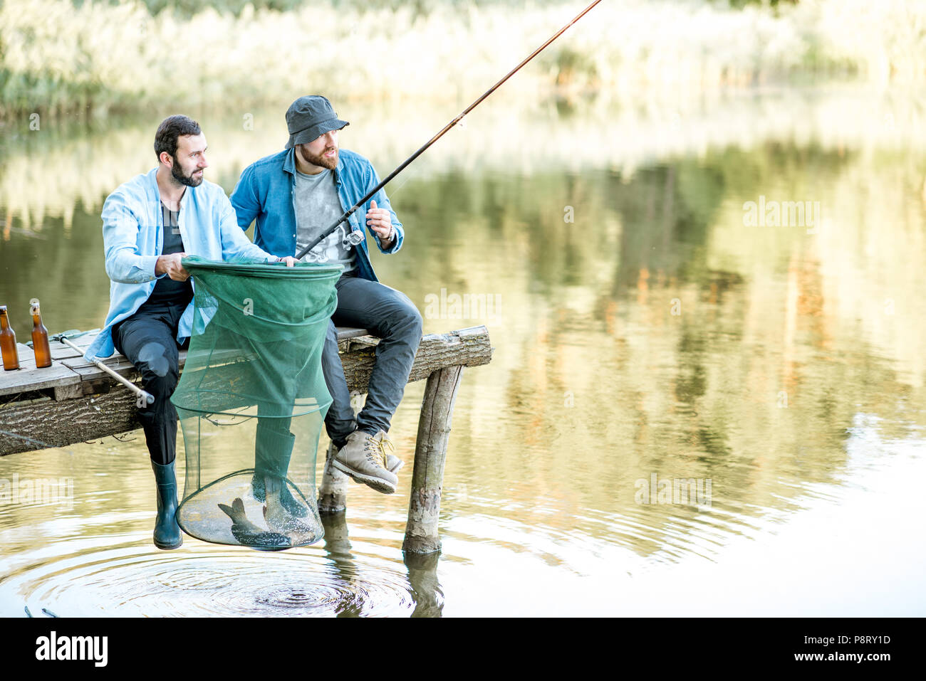 Due felici amici maschi guardando la rete da pesca con pesce durante la pesca sul lago Foto Stock