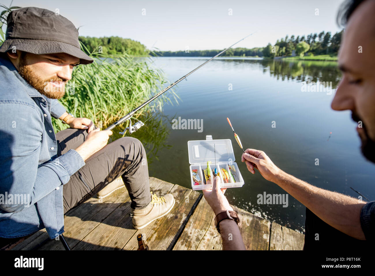 Due uomini con la pesca affronta durante il processo di pesca sul lago al mattino Foto Stock