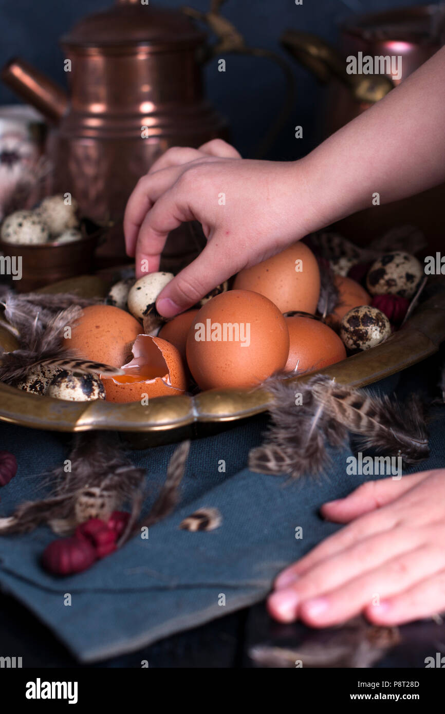 I bambini con le mani in mano nel telaio, le uova di Pasqua di grandi e piccole dimensioni, piume. Foto in stile vintage. Accessori rurale. Spazio di copia Foto Stock