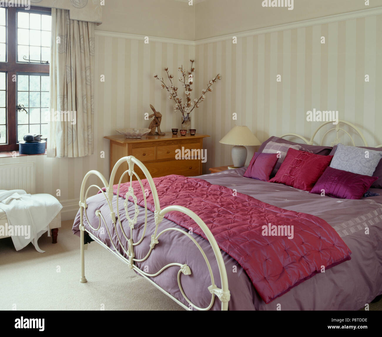 Rosa luminoso cuscini di seta e di gettare sul ferro bianco letto con trapunta malva in camera bianca Foto Stock