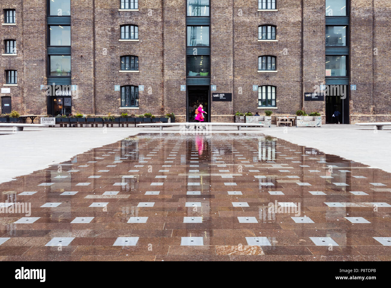 Basso angolo di ripresa dell'Università delle Arti di Londra (UAL) in Piazza Granaio, King's Cross, che mostra una donna con un cappotto rosa posizionata centralmente Foto Stock