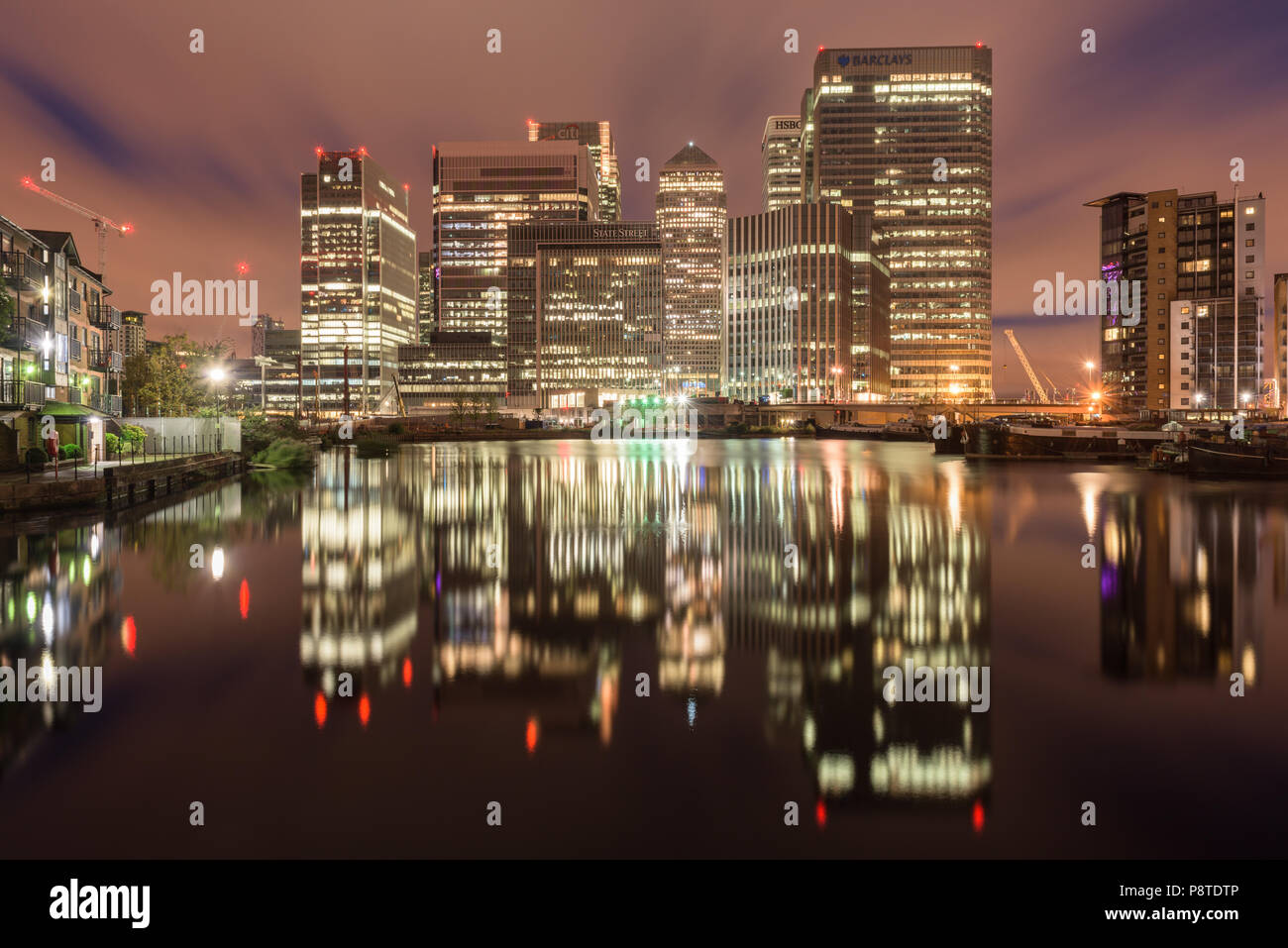 A tarda notte riflessioni dell'illuminato edifici per uffici di Canary Wharf, Londra, preso dal bacino di Blackwall Foto Stock