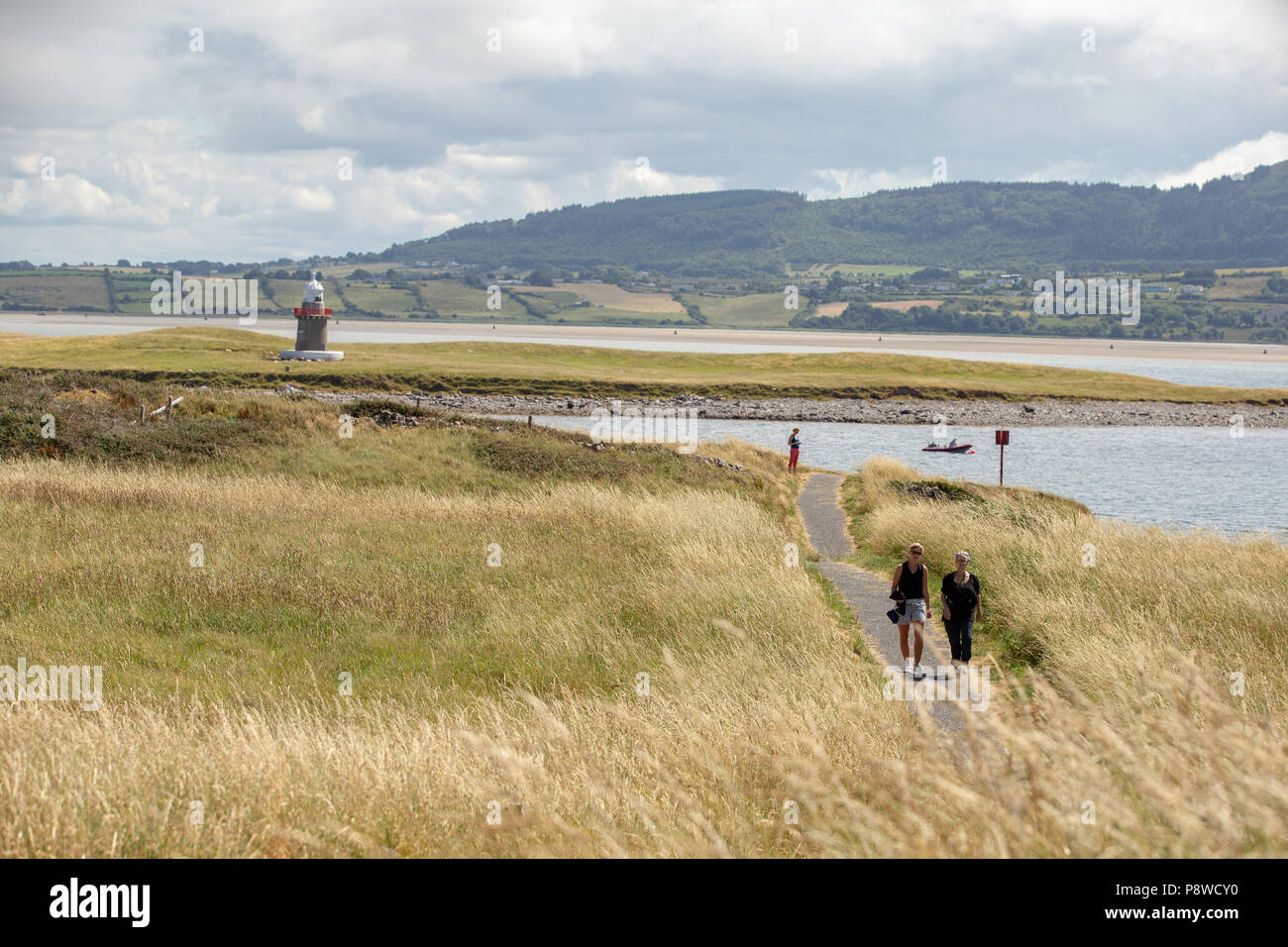 I turisti a piedi lungo il Rosses Point via costiera trail con ostriche Island e il suo famoso faro in background su una soleggiata giornata estiva. Foto Stock
