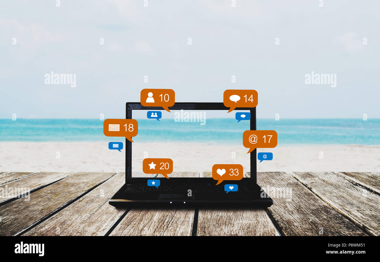 Computer portatile sul tavolo di legno in spiaggia in estate con i social media e social network le icone di notifica Foto Stock