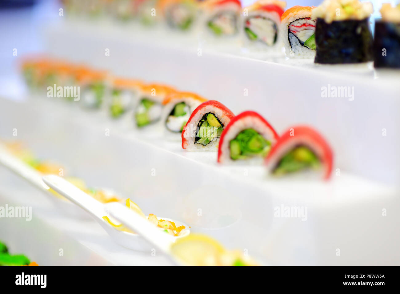 Delizioso sushi con topping di avocado su laminati piatti di pesce e di riso disposti in una fila su un vassoio in corrispondenza di un evento di catering Foto Stock