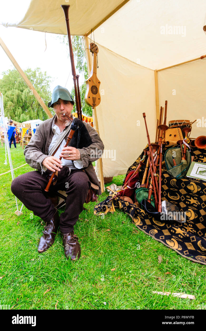 Rievocazione storica, storia vivente evento. Uomo caucasico in costume medievale di un menestrello, seduti all'aperto e tenendo cornamuse. Foto Stock
