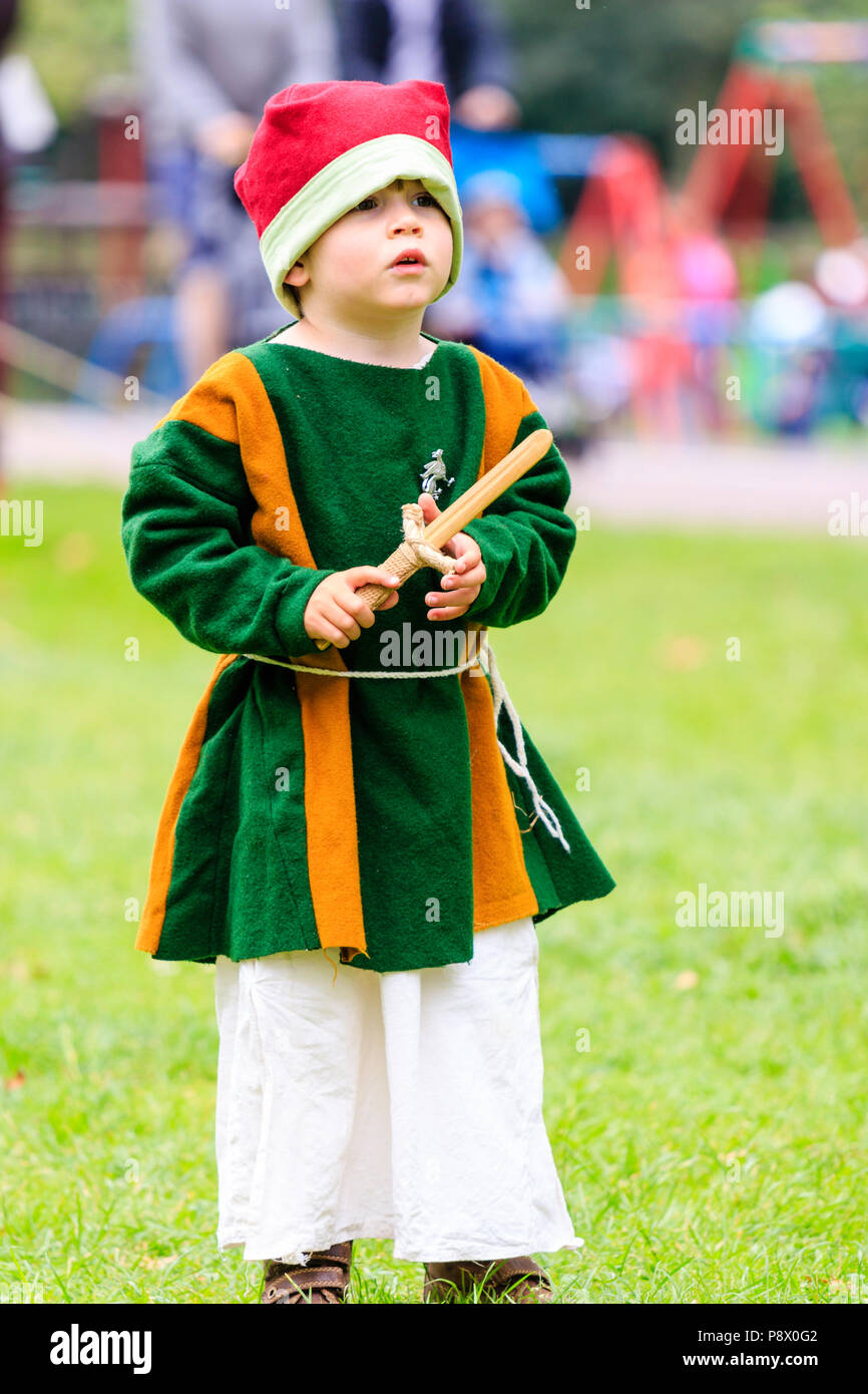 Bambino, ragazzo, 3-4 anni, in costume medievale durante la storia vivente rievocazione storica evento. Azienda pugnale in legno, mentre in piedi all'aperto sull'erba. Foto Stock