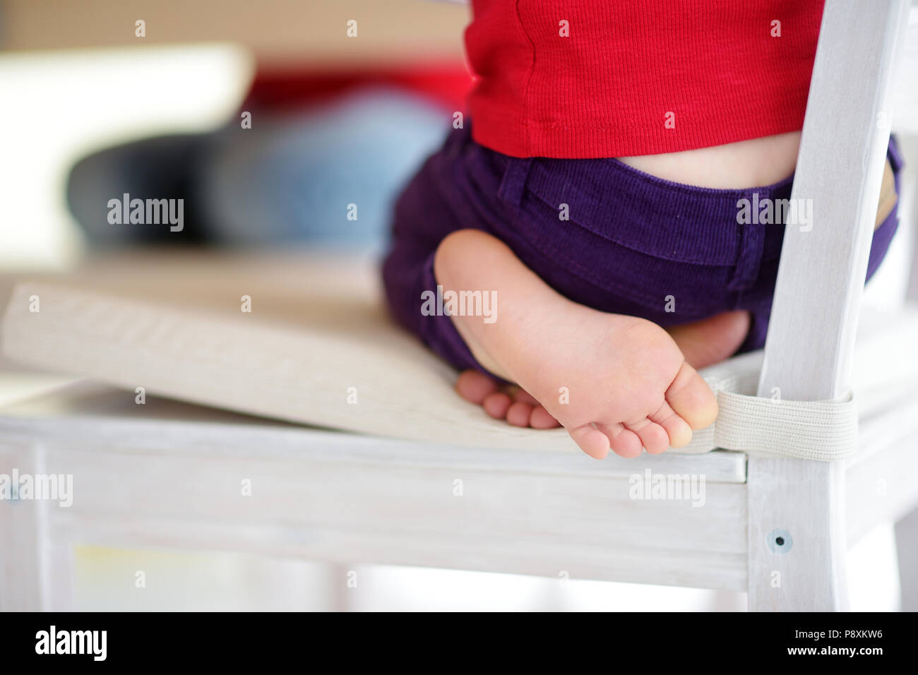 Carino poco i piedi di un bambino seduto su una sedia in cucina bianca Foto Stock