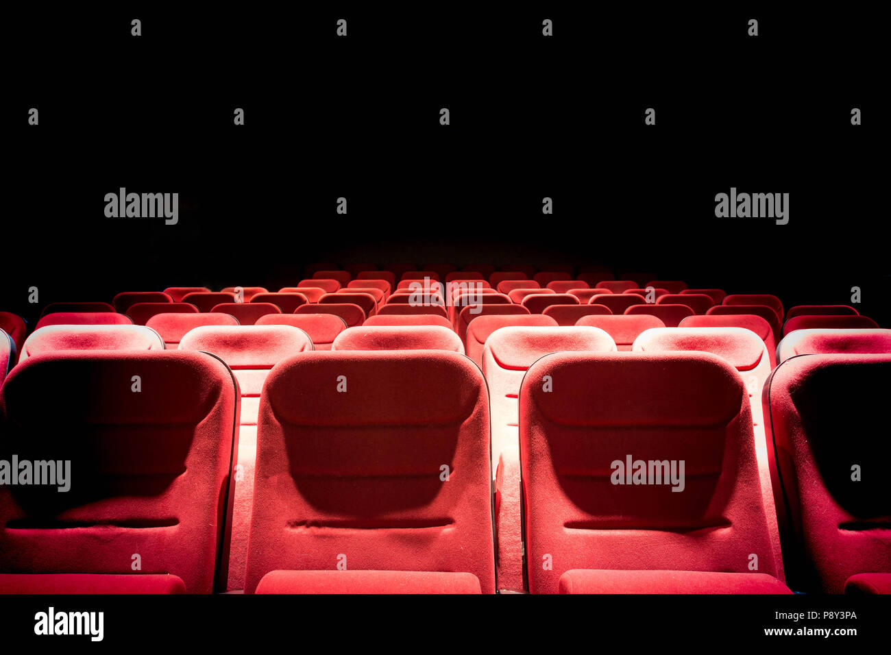 Scuri cinema con luce di proiezione e vuoto sedili rosso Foto Stock