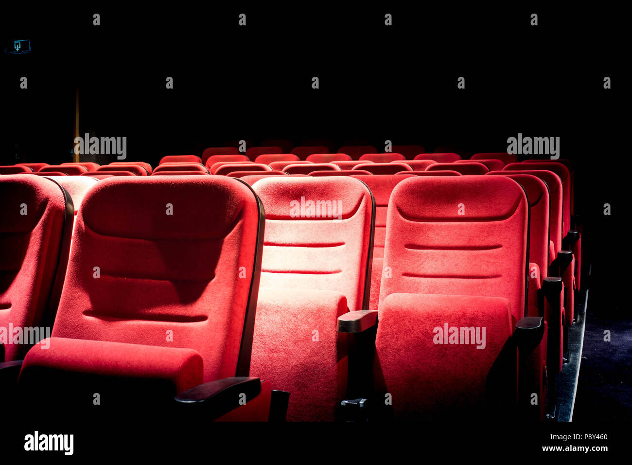 Scuri cinema con luce di proiezione e vuoto sedili rosso Foto Stock
