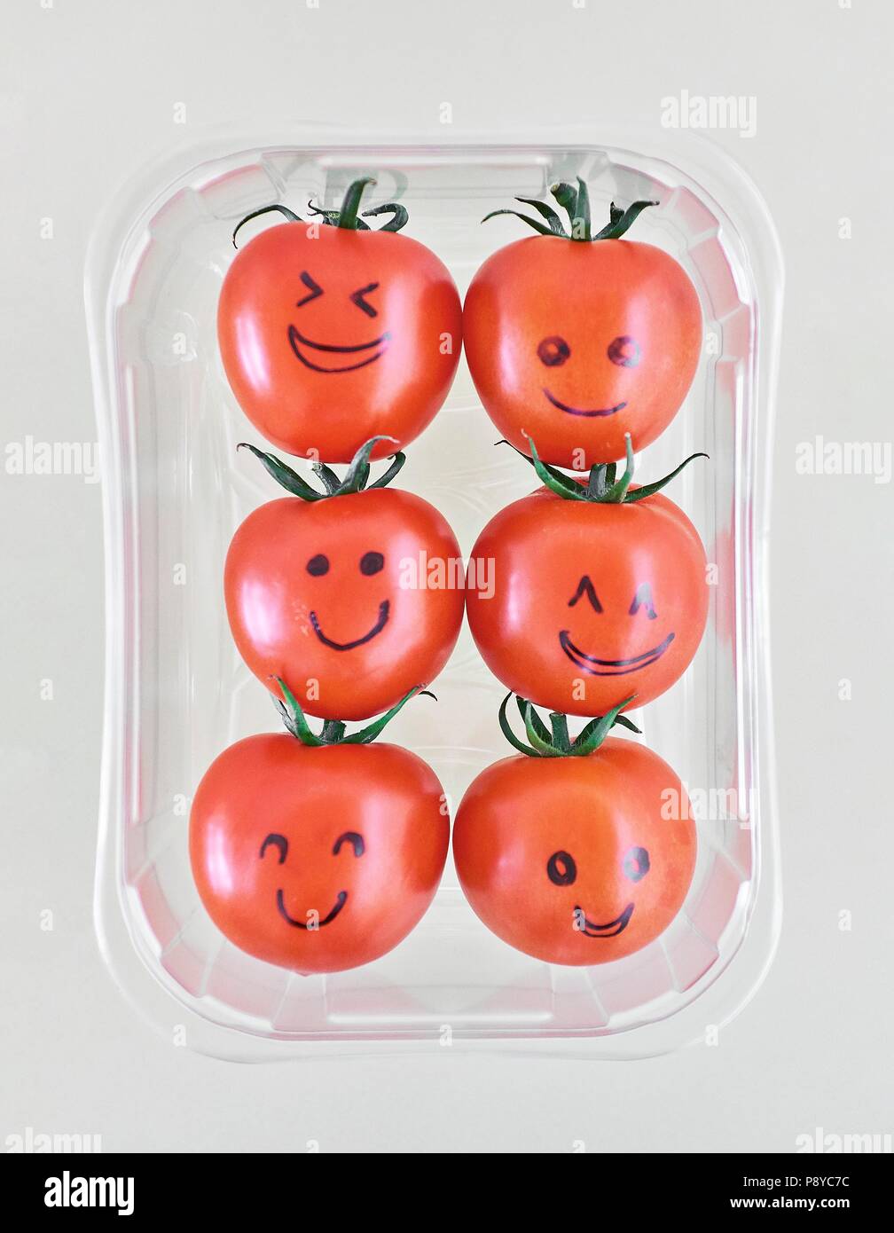 Sei pomodori con occhi e bocca disegnati in inchiostro nero in contenitore di plastica. Foto Stock