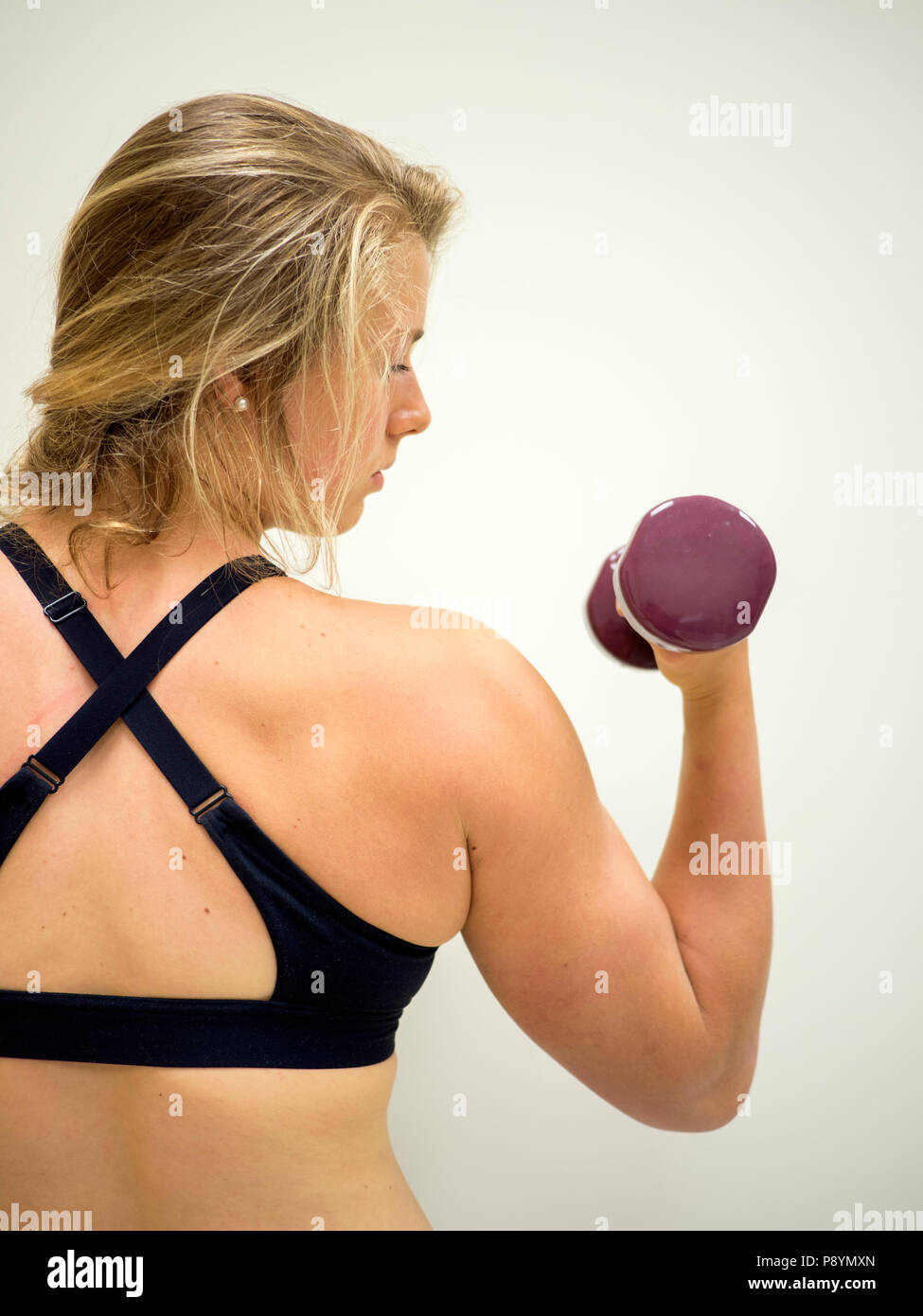Forte donna femmina facendo bicipite riccioli guardando il peso nel suo braccio Foto Stock
