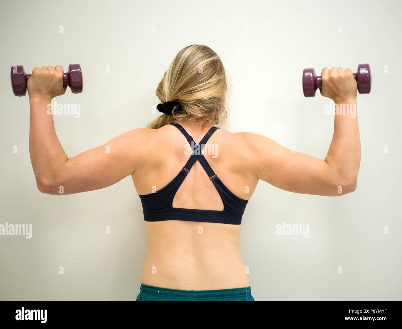 Forte femmina bianco facendo esercizi a lavorare al suo bicipite e muscoli della spalla con pesi Foto Stock