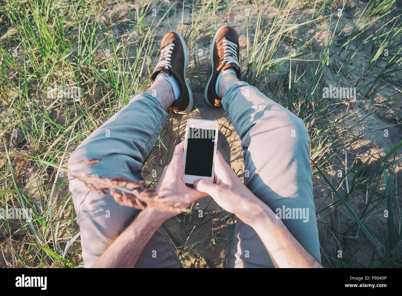 Foto all'aperto dell'uomo seduto sull'erba tenendo il telefono con schermo vuoto. Foto Stock