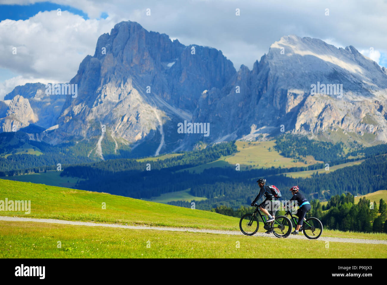 I turisti in bicicletta in Alpe di Siusi, il più grande ad alta altitudine prato alpino in Europa, incredibili montagne rocciose sullo sfondo. Alto Adige Provincia di Foto Stock