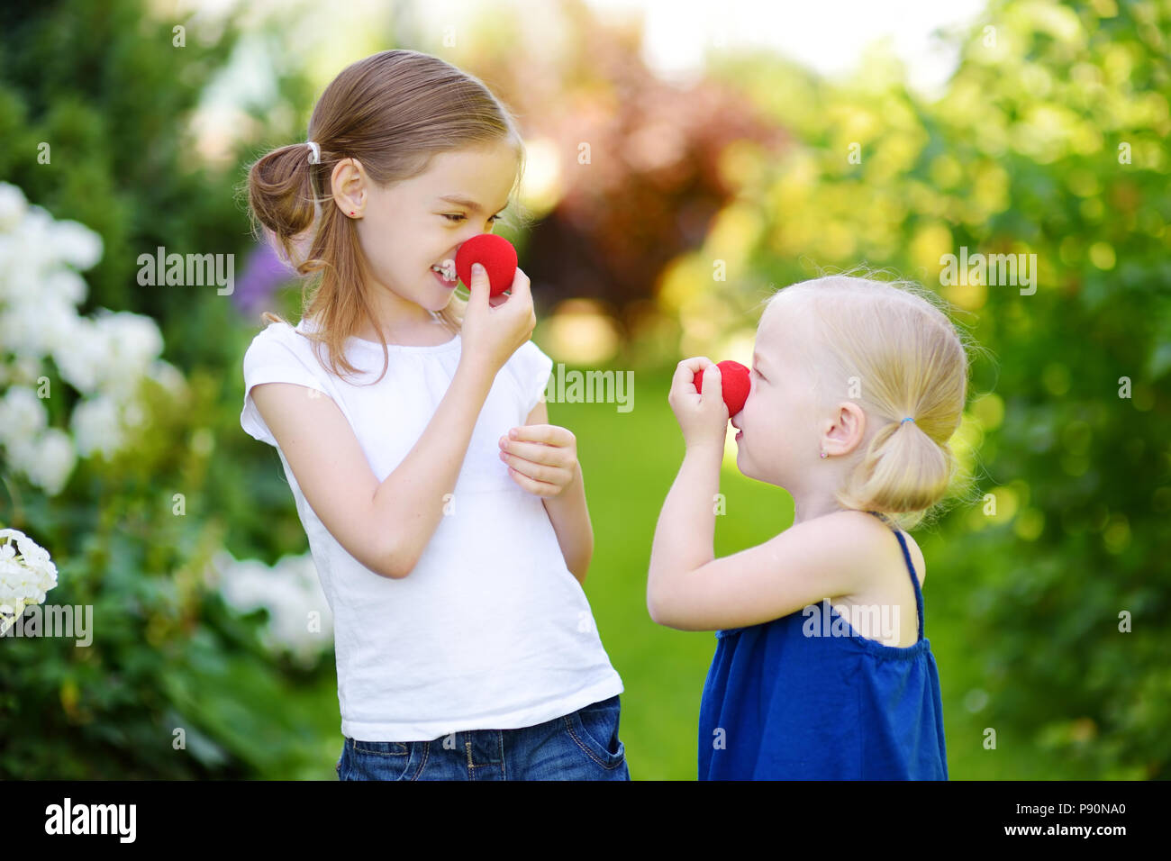 Felice piccole sorelle indossando red clown naso divertirsi insieme sulla soleggiata giornata estiva all'aperto Foto Stock
