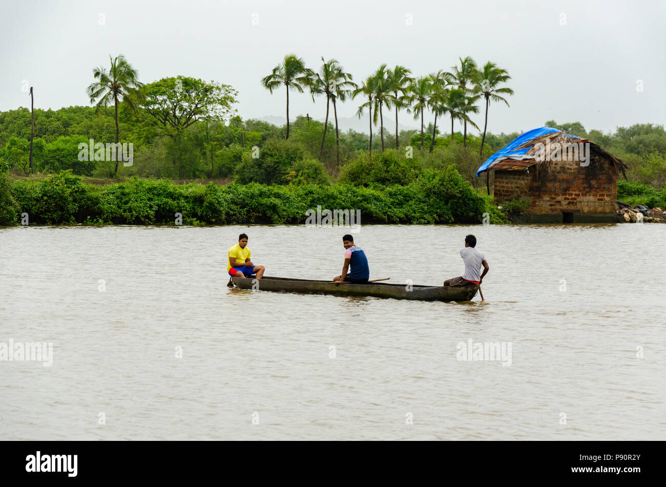 Tre uomini su una canoa che va al di là del fiume Sal backwaters come visto da Joe's River Cove, Cavelossim, Goa, India Foto Stock