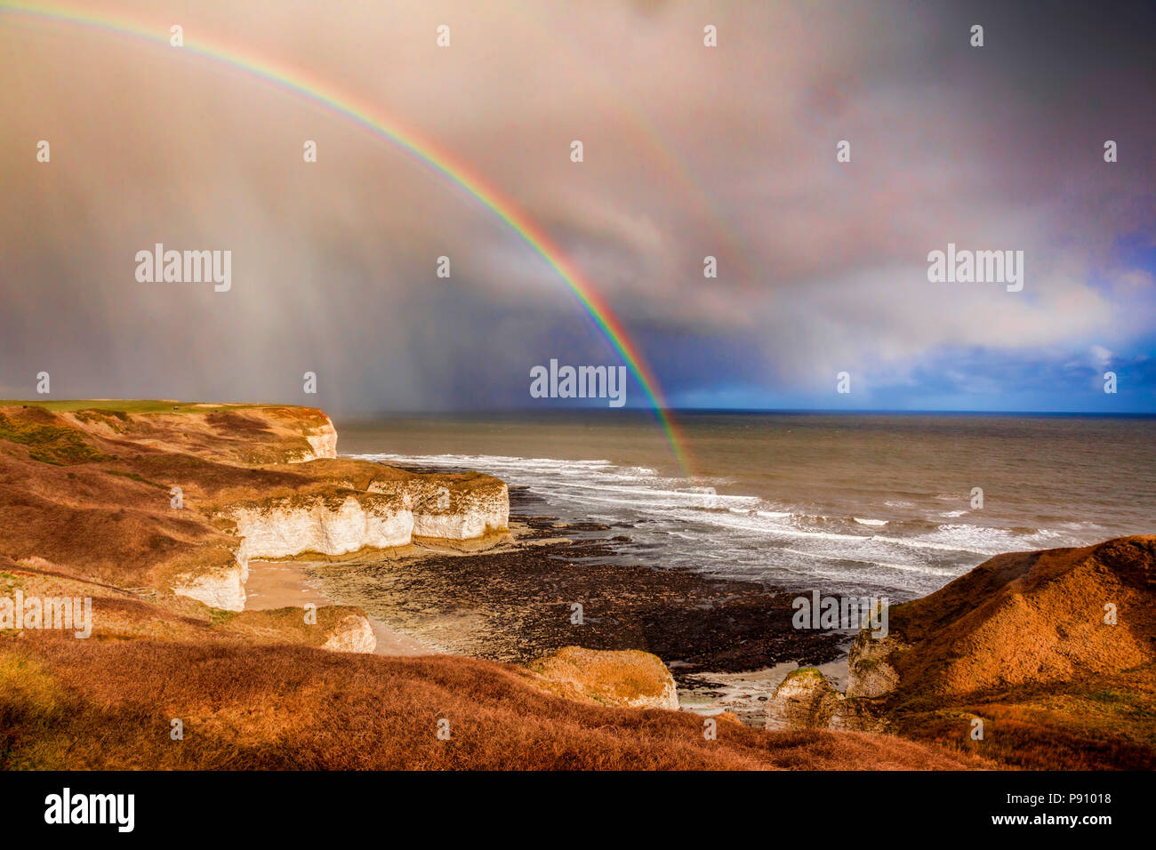 Condizioni atmosferiche variabili sopra le scogliere calcaree di Flamborough Head, East Yorkshire, Inghilterra, Regno Unito, come un avvicinamento doccia di pioggia porta un arcobaleno. Foto Stock