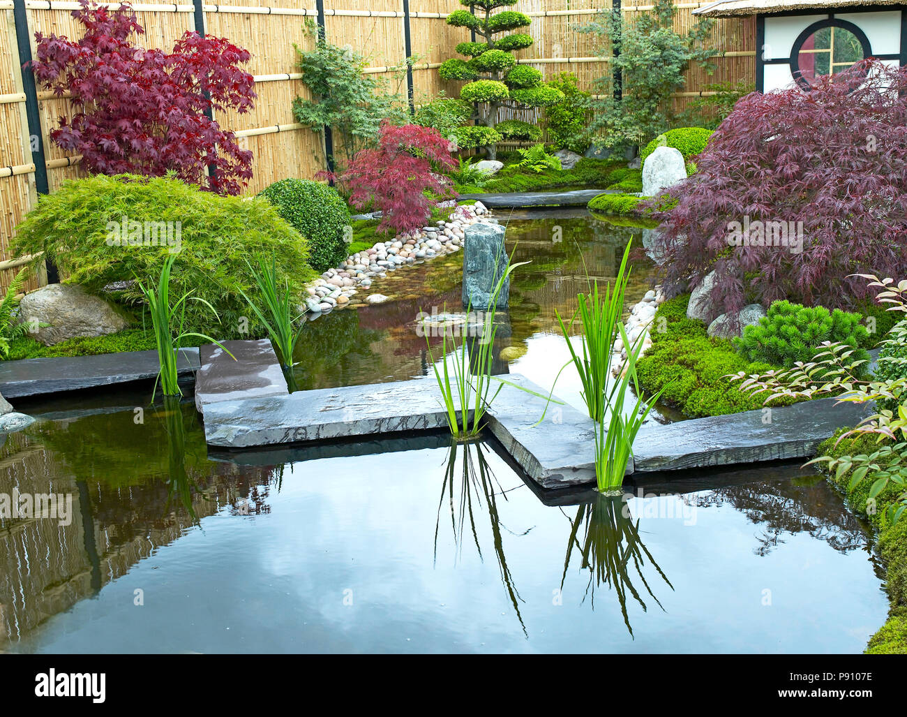 Tradizionale Giapponese del acqua giardino con piante, arbusti, rocce, Tea House e il ponte di pietra Foto Stock