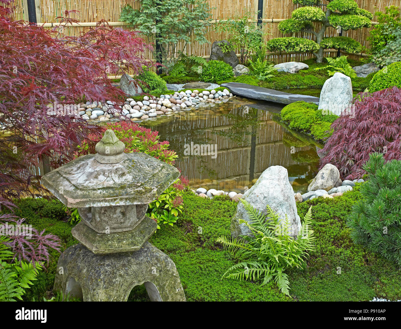 Tradizionale Giapponese del acqua giardino con piante, arbusti, rocce e lanterna di pietra Foto Stock