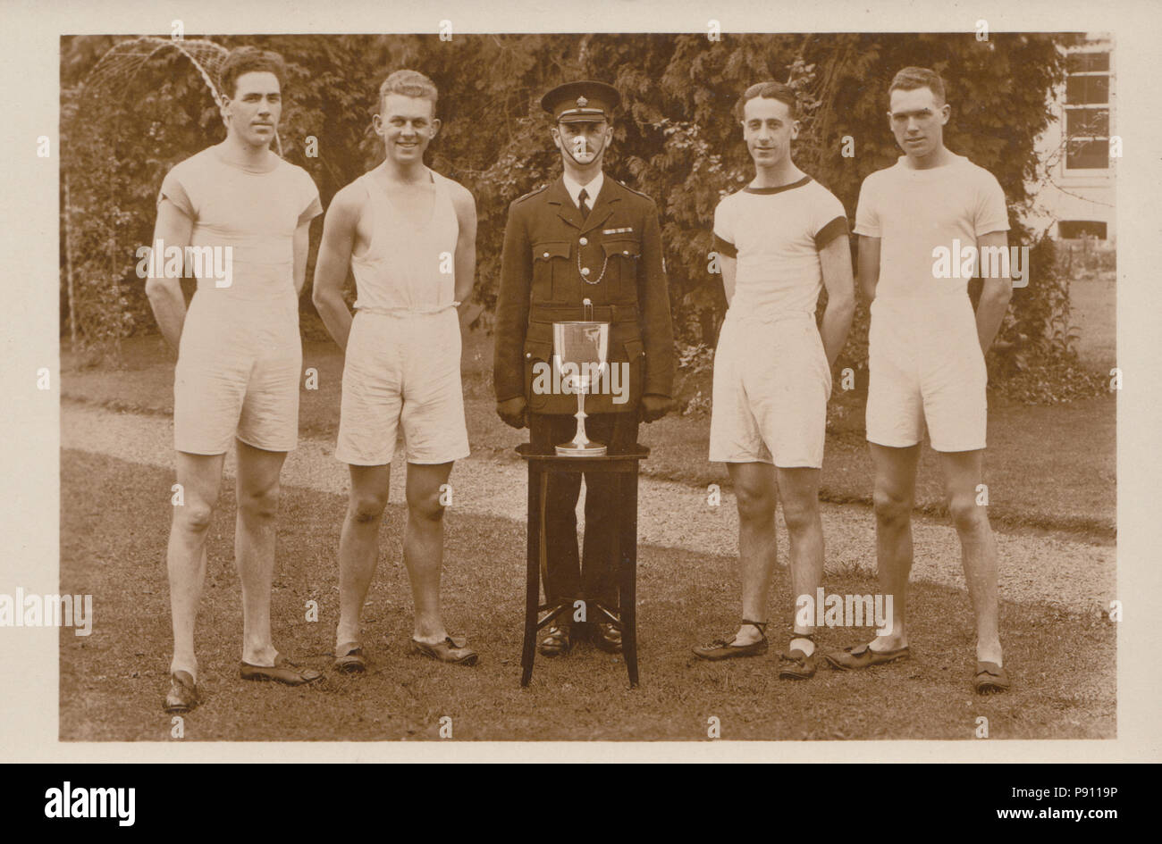 Vintage fotografia di un relè di atletica team con il suo trofeo. Funzionario in uniforme anche presente. Foto Stock