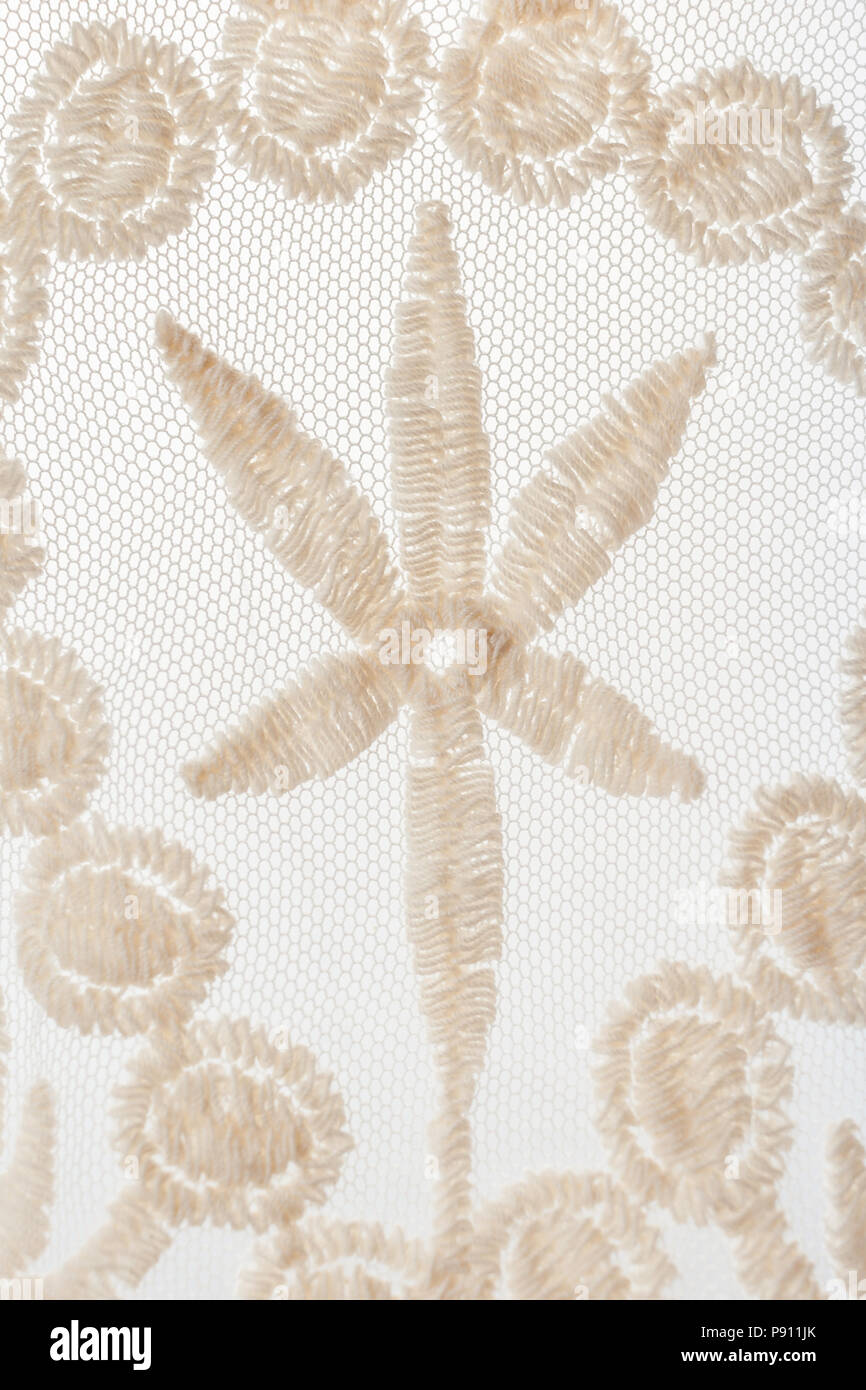 Close-up parte della maglia in pizzo beige con motivo floreale su sfondo bianco. Messa a fuoco selettiva. Foto Stock