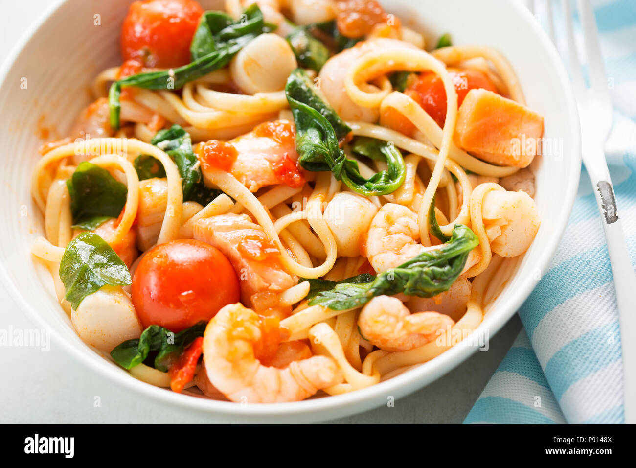 Frutti di mare linguine con gamberetti, capesante e salmone, spinaci e pomodori Foto Stock