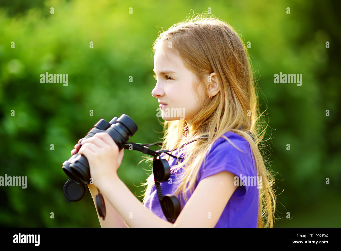 Funny bambina guardando attraverso il binocolo su soleggiate giornate estive. Bambino esplorare viste distanti. Foto Stock