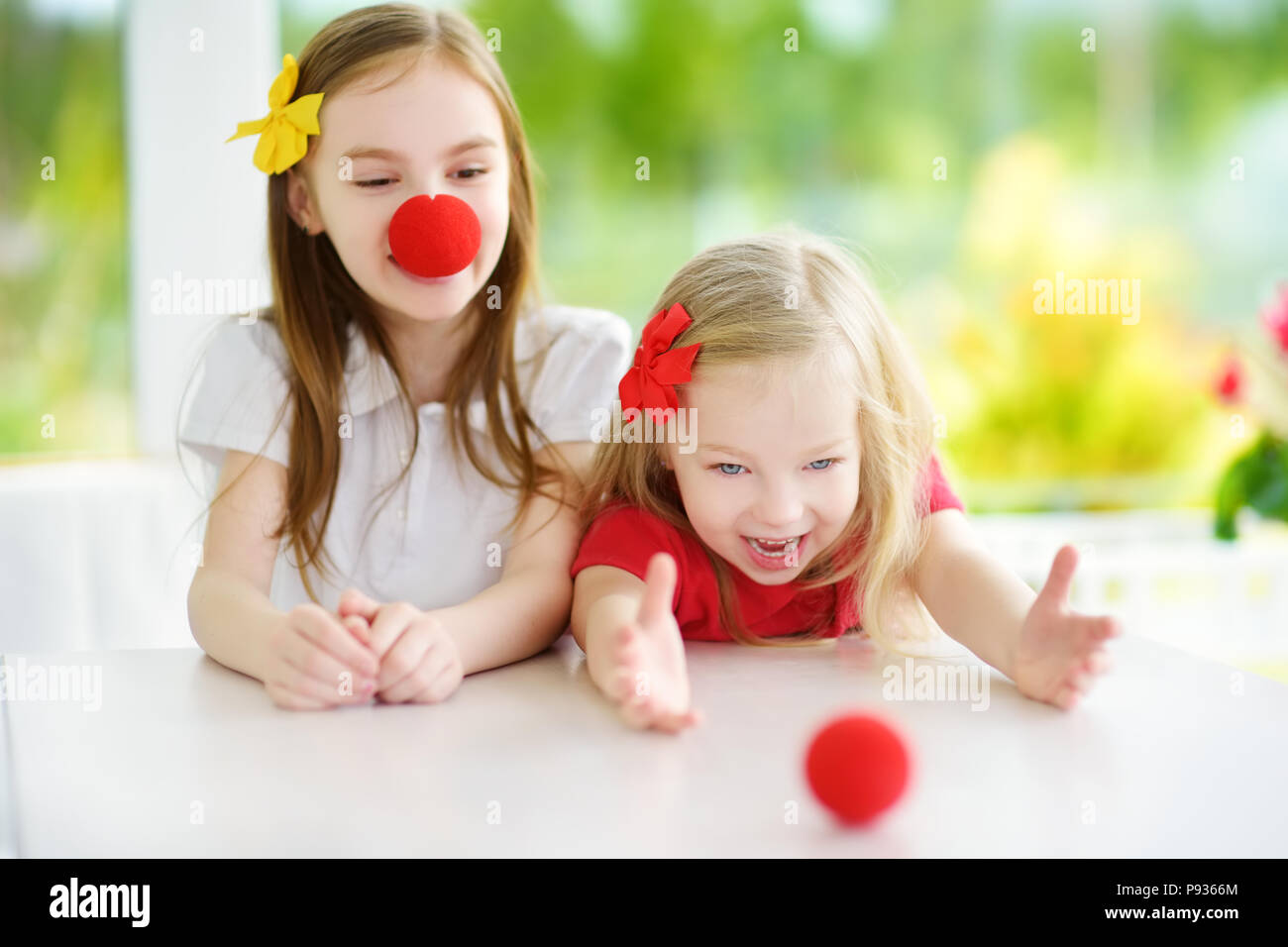 Felice piccole sorelle indossando red clown naso divertirsi insieme sulla soleggiata giornata estiva a casa. Due bambini che giocavano insieme. Foto Stock