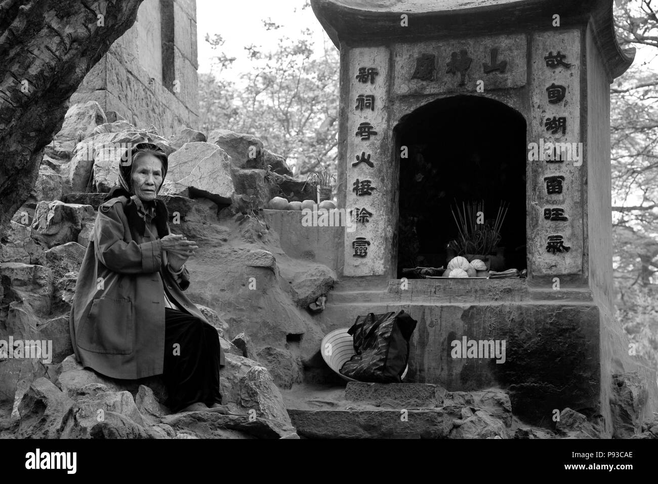 Un'anziana donna vietnamita si siede alla base dell'NGOC SON TEMPLE nel vecchio quartiere - Hanoi. Il Vietnam Foto Stock