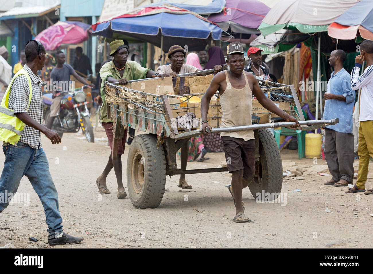 Kakuma, Kenya - Tageloehner tirare un grande rimorchio di trasporto caricata con merci su un occupato, strada sterrata. Foto Stock