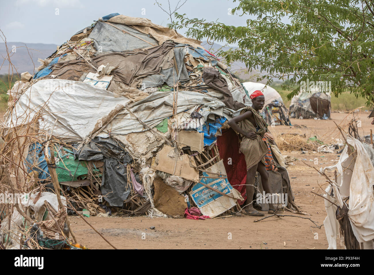 Kakuma, Kenya - Sul bordo del campo profughi di Kakuma. Un giovane uomo si pone di fronte alla sua capanna coperto con vecchi teloni di plastica, coperte e scatole di cartone. Foto Stock