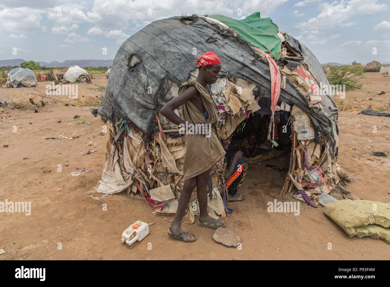 Kakuma, Kenya - Sul bordo del campo profughi di Kakuma. Un giovane uomo si pone di fronte alla sua capanna coperto con vecchi teloni di plastica, coperte e scatole di cartone. Foto Stock