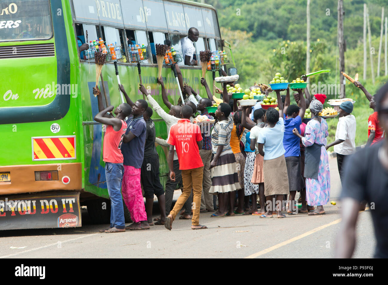 Kamdini, Uganda - ad una fermata del bus, battenti mercanti offrono ai viaggiatori un " commuter " bus per la vendita. Foto Stock