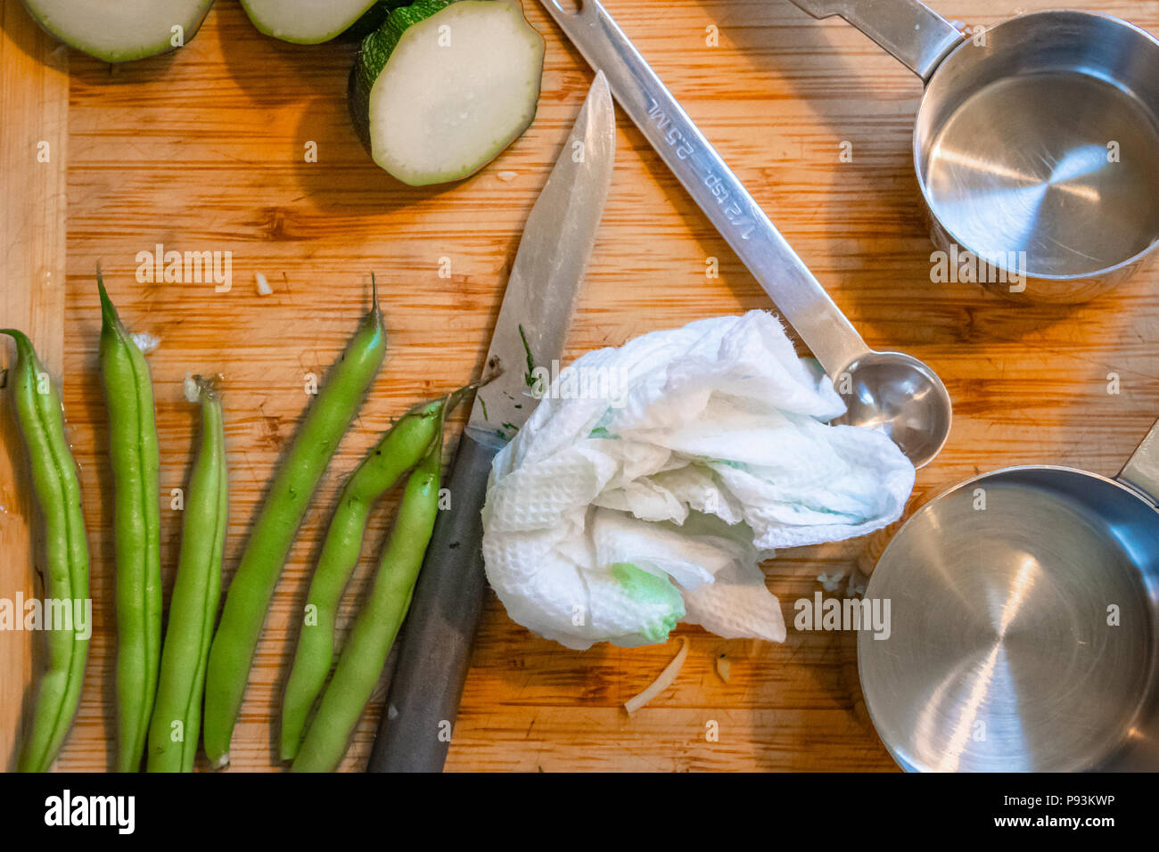 Cetrioli, fagioli verdi, utensili di misurazione e un coltello giacciono su di un tagliere di legno durante la preparazione del cibo. Foto Stock