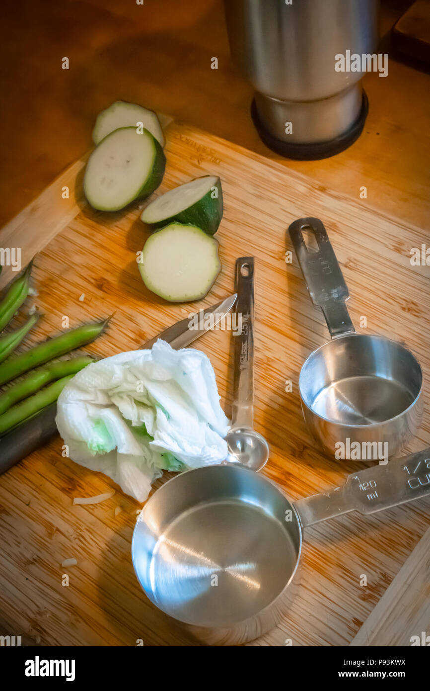 Cetrioli, fagioli verdi, utensili di misurazione e un coltello giacciono su di un tagliere di legno durante la preparazione del cibo. Foto Stock