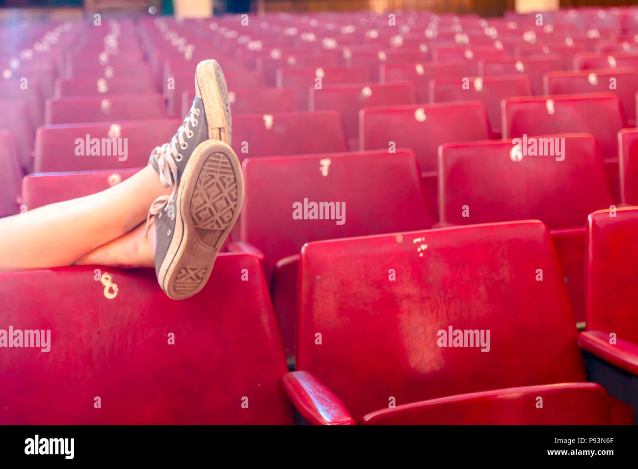 Una lunga esposizione foto, giovane donna in posa con gambe incrociate nel teatro vuoto. Foto Stock