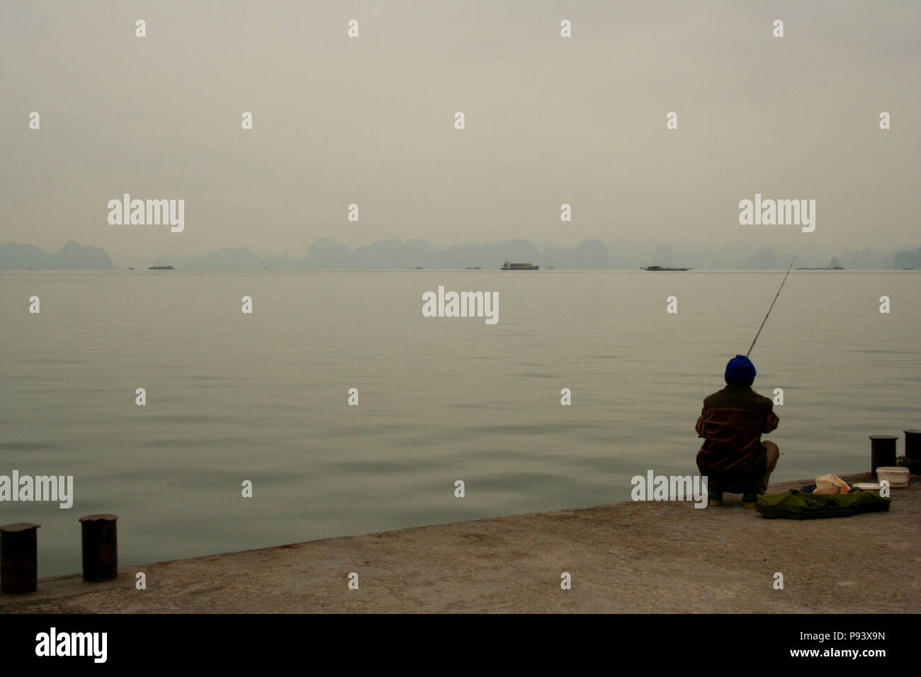 Pescatore solitario a pesca di Halong Bay con barche e pinnacoli di calcare in background, Vietnam Foto Stock