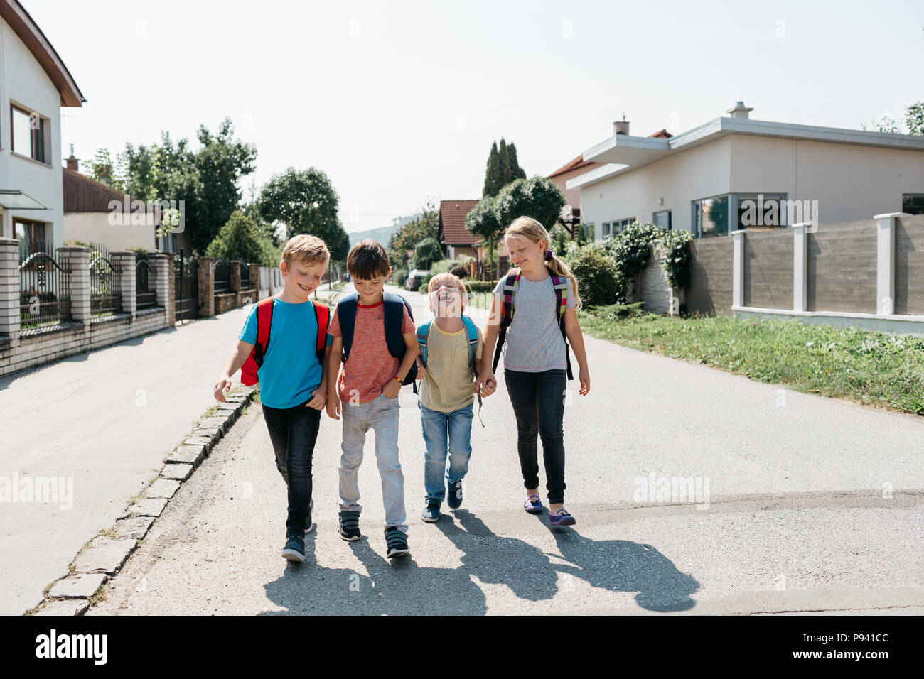 Bambini primario a piedi in strada il loro primo giorno di scuola. Un gruppo di compagni di scuola felice andare a scuola a piedi sul proprio divertimento. Foto Stock