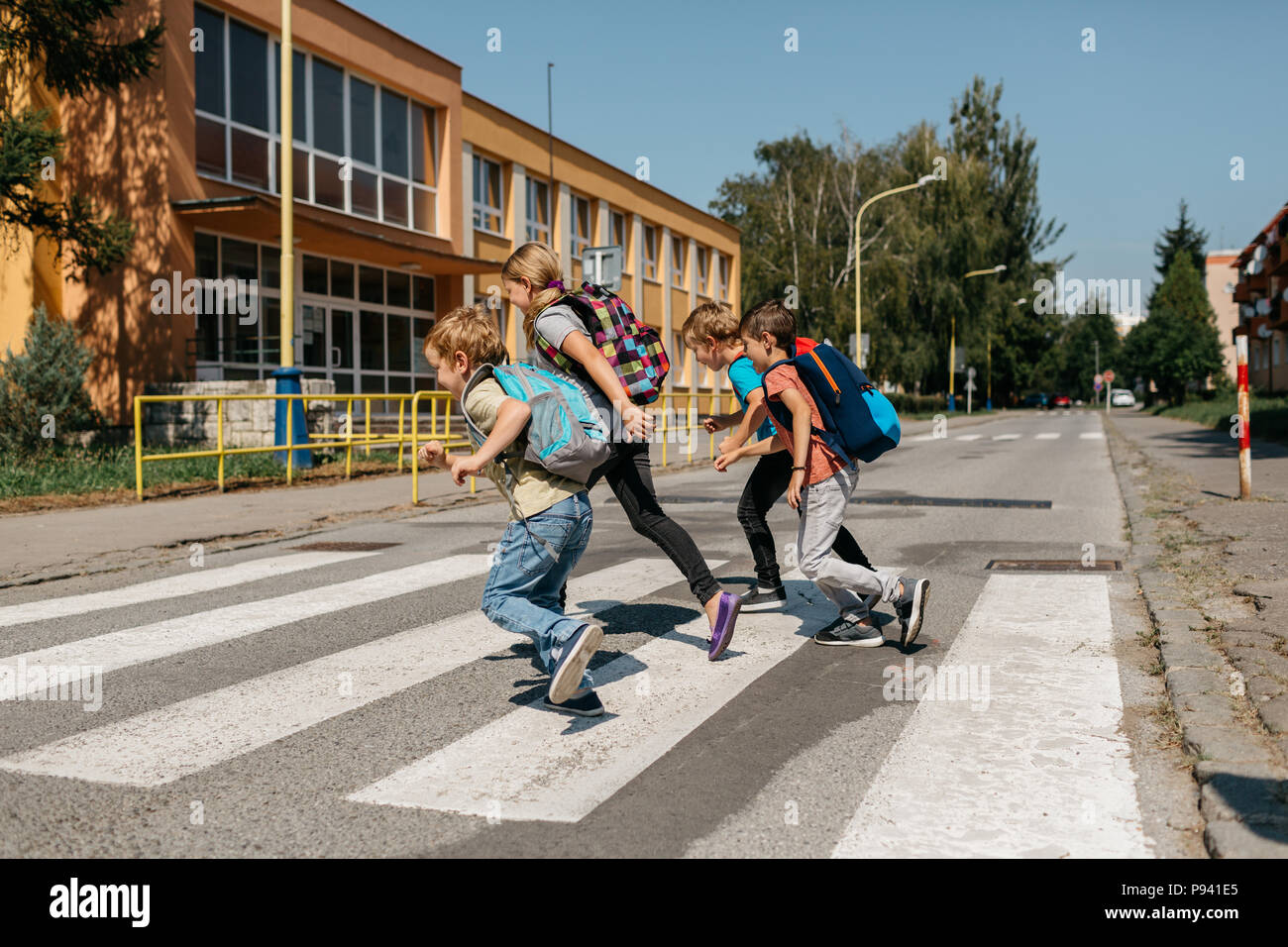 I bambini della scuola di corsa attraverso una strada in un crosswalk. Gruppo di studenti primari correndo a scuola. Foto Stock