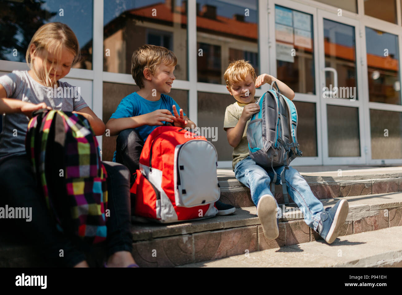Allegro scuola bambini durante una pausa. Bambini sorridenti con schoolbags seduti sulle scale al di fuori della scuola. Foto Stock