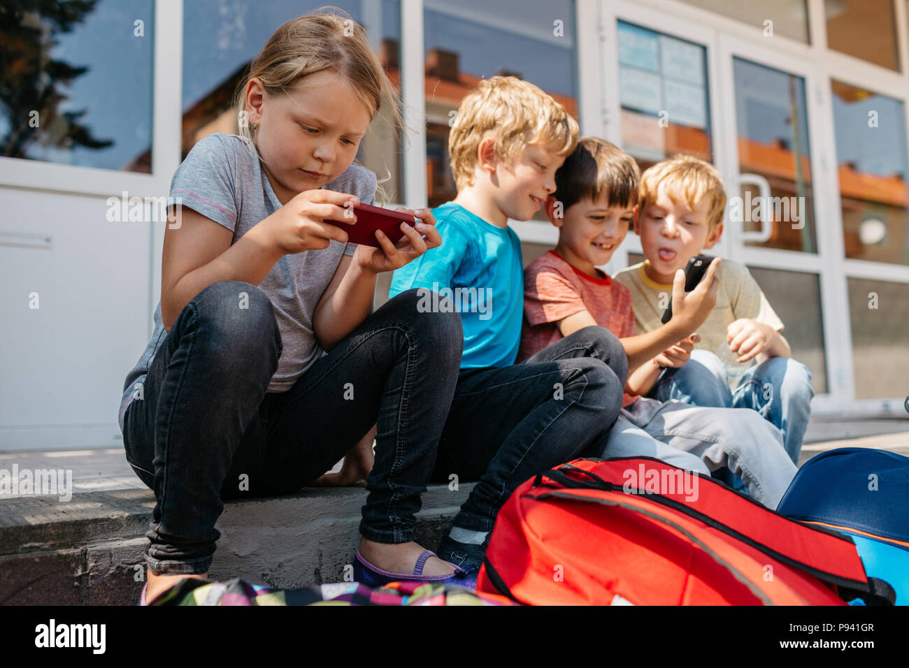 I bambini seduti sulle scale di fronte scuola la navigazione sul web. Scolari divertirsi giocando con il cellulare durante una pausa. Foto Stock