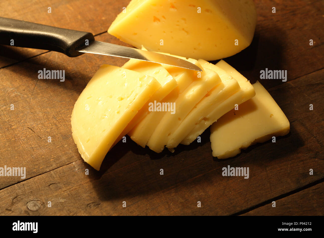 Formaggio a fette e coltello giacente su sfondo di legno Foto Stock