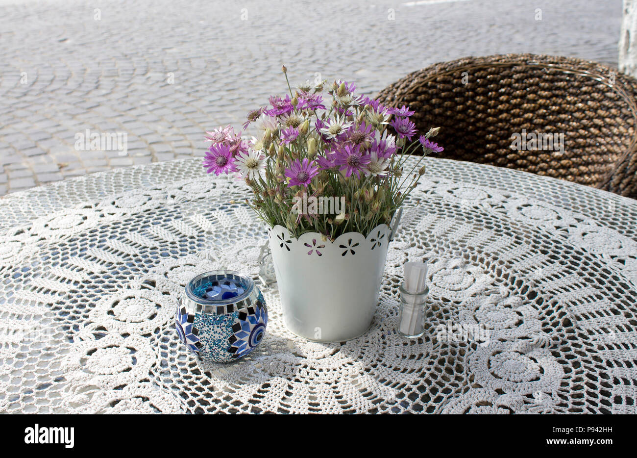 Foto di intimo cafe tabella sulla pavimentazione in pietra street nella soleggiata mattinata estiva con splendidi fiori sulla tovaglia di pizzo e poltroncina in legno. Foto Stock