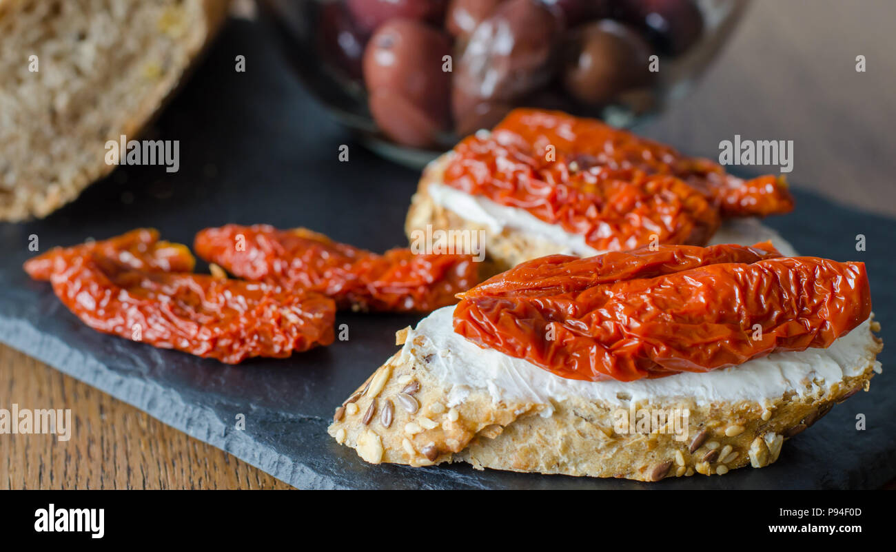 Bruschetta con pomodori secchi e formaggio a pasta morbida con ebollizione di olive. La cucina tradizionale italiana sandwich. Antipasti Foto Stock