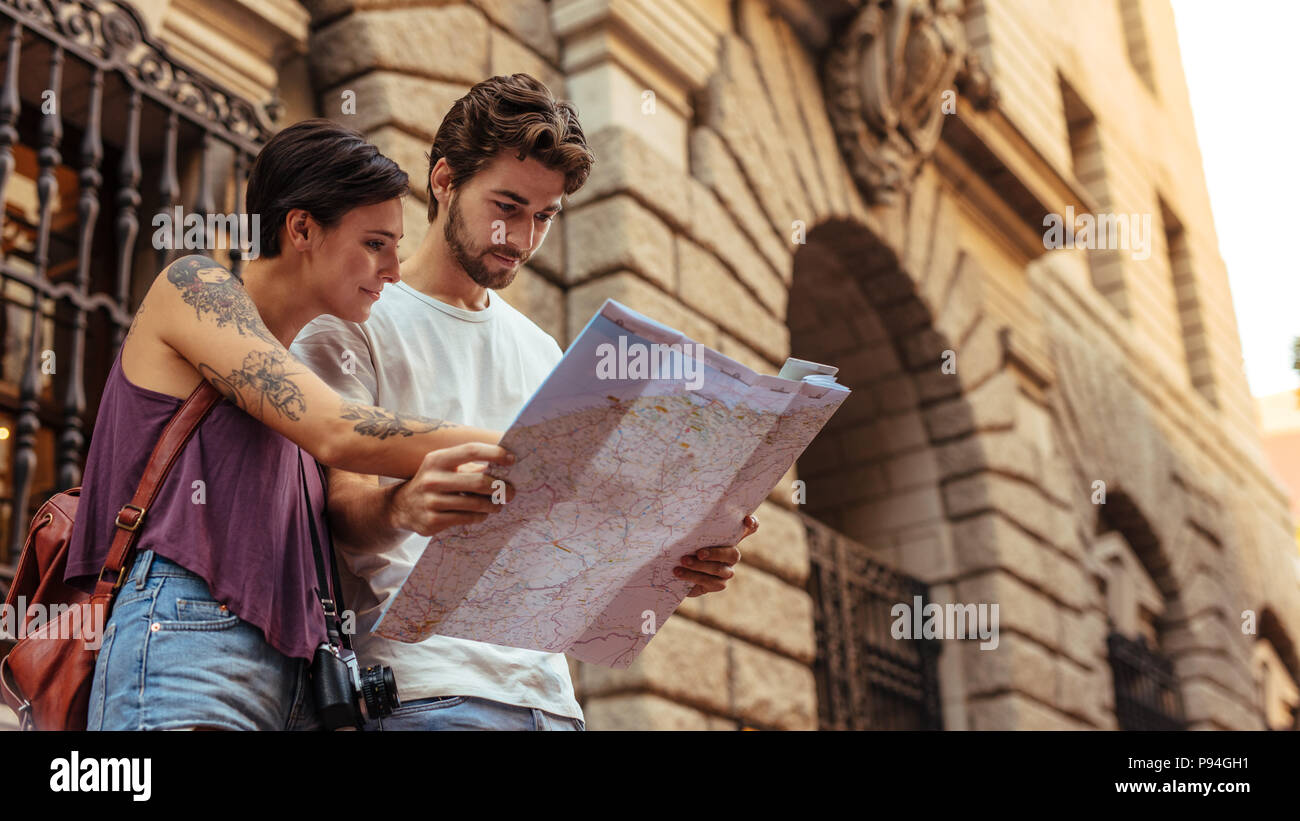 Turista giovane utilizzando una mappa per trovare il percorso verso la loro destinazione. L uomo e la donna i viaggiatori in piedi vicino a un vecchio edificio in pietra. Foto Stock