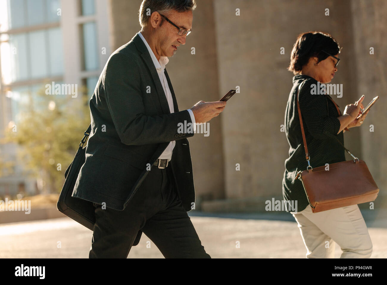 Uomo e donna che utilizza il cellulare mentre il pendolarismo per office su una strada della citta'. La gente di affari di controllare le loro telefono cellulare mentre si cammina a office showi Foto Stock