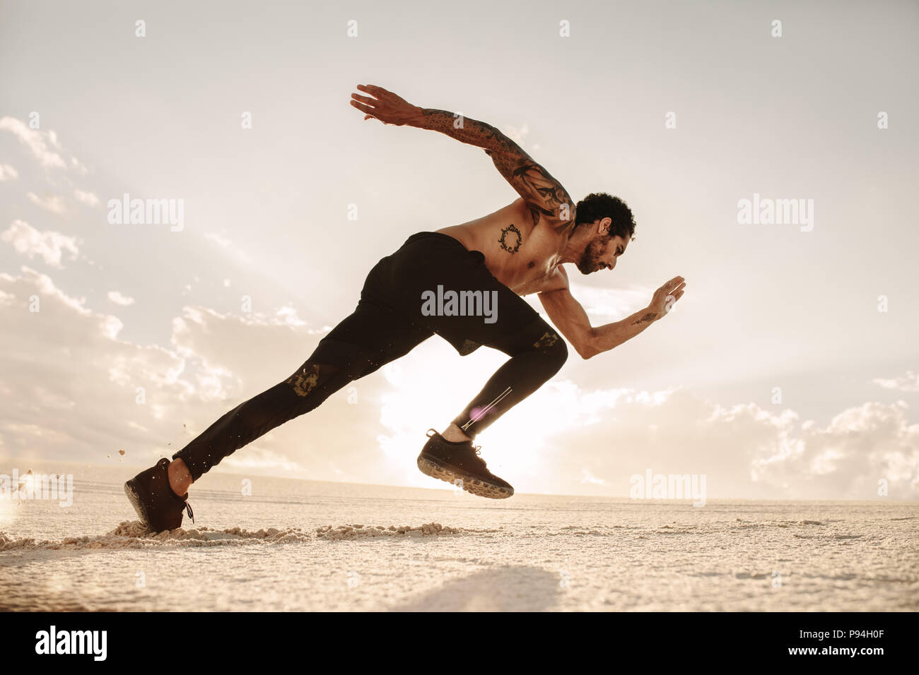 Giovane atleta maschio lanciando off per una corsa sulla sabbia del deserto. Runner in esecuzione sulla duna di sabbia. Foto Stock