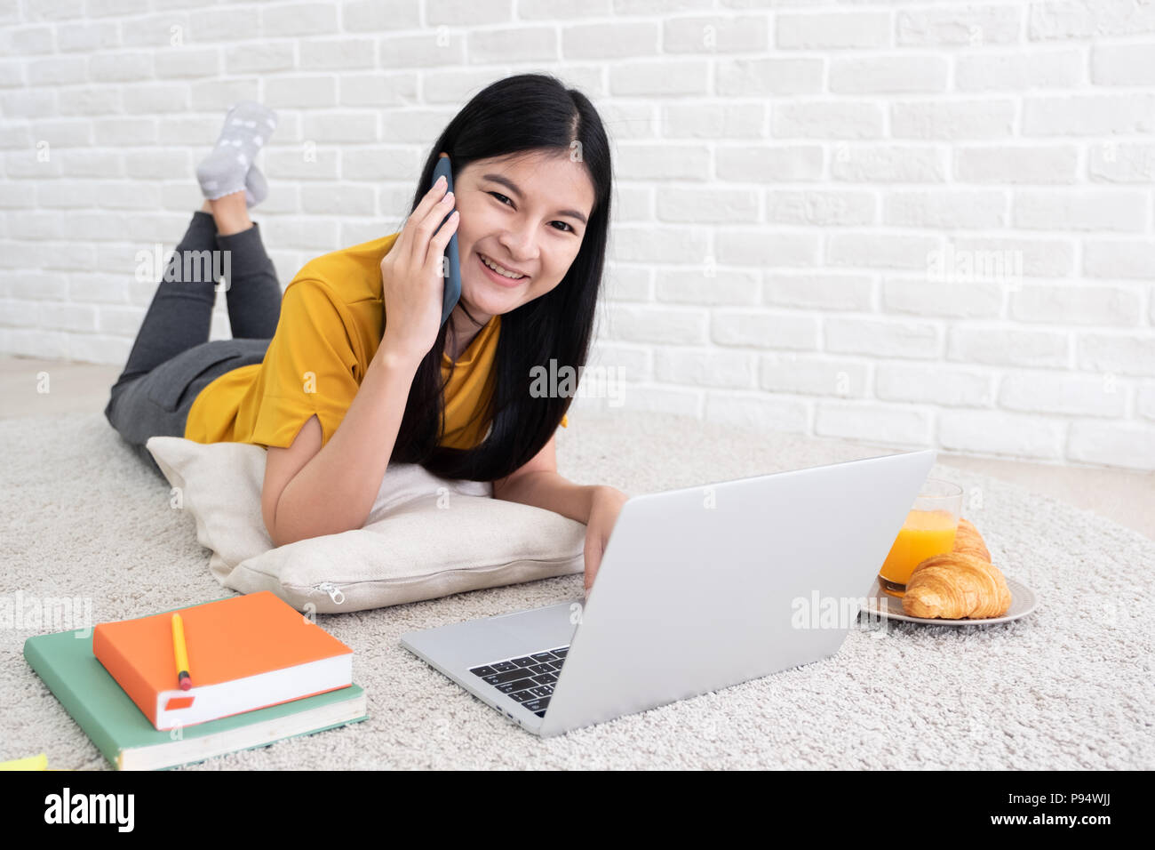 Femmina asiatici parlare sul mobile e di utilizzare il computer portatile per il lavoro a casa.la donna stabiliscono sul tappeto a muro di mattoni.lavorando stile di vita on line Foto Stock