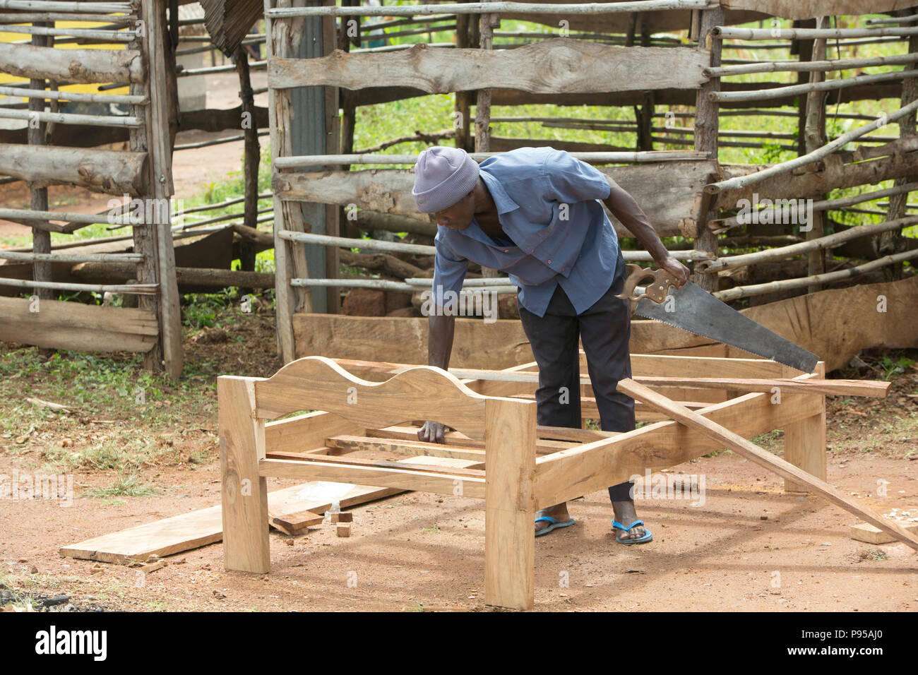 Kamdini, Uganda - un falegname moquette un letto in legno sul ciglio della strada. Foto Stock